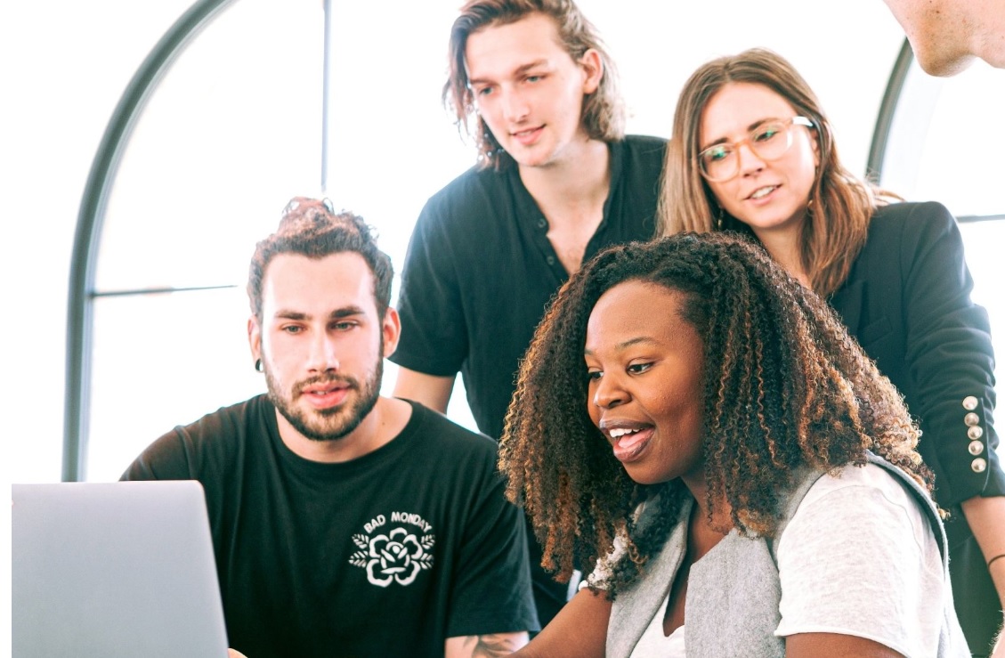Marketing de comunidade: Um grupo de pessoas estão acompanhando uma moça negra que apresenta algo na tela de um computador.