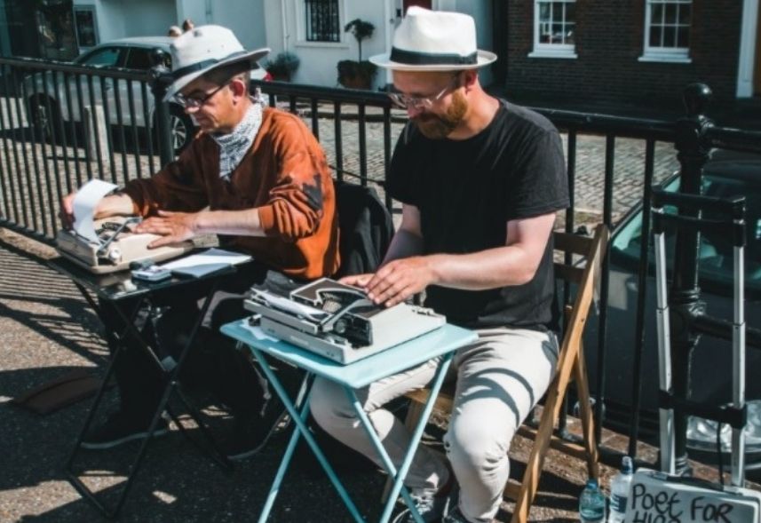 O que e copywriting: duas pessoas brancas estão sentadas em duas mesas separadas. Sobre as mesas estão máquinas de escrever e cada um está digitando um conteúdo. Essa imagem está sendo utilizada para ilustrar o post "o que é copywriting".