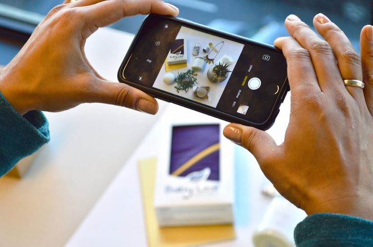 Anúncios nos Stories do Instagram: imagem de duas mãos segurando o celular tirando foto de uma mesa cheia de produtos