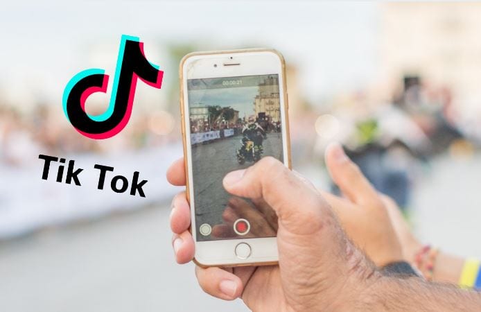 Como fazer vídeo no Tik Tok: imagem de uma mão gravando um vídeo no celular com o logo ao aplicativo Tik Tok