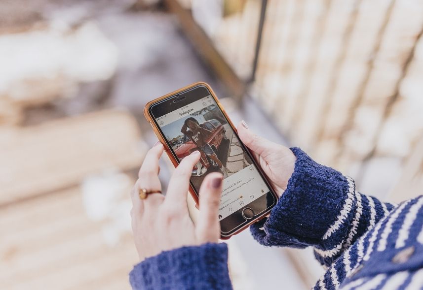 Como marcar pessoas no Instagram: imagem de uma mulher segurando o celular com uma mão e com a outra mão tocando na tela do Instagram