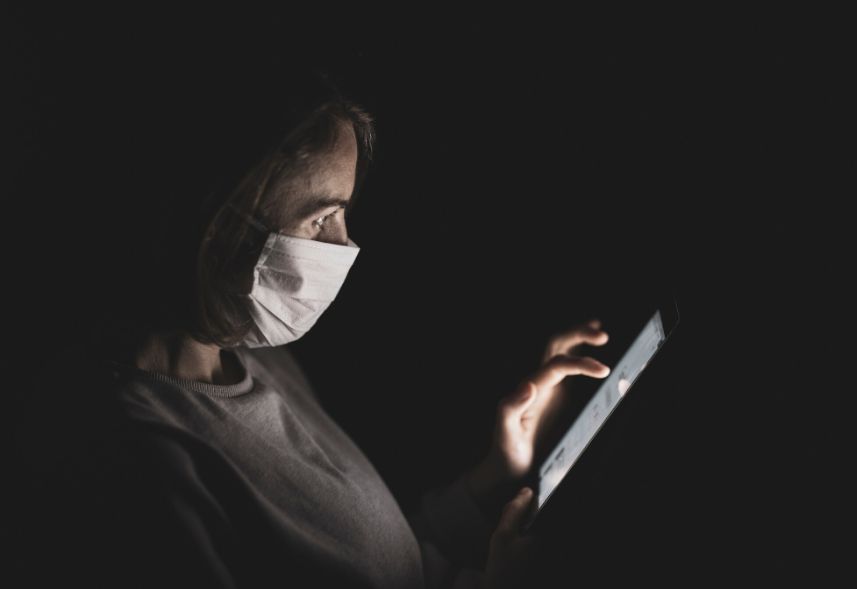 Comunicação em tempo de crise: imagem de uma mulher usando uma máscara branca no rosto mexendo no celular