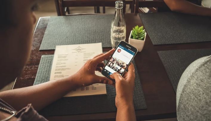 Deixar de seguir no Instagram: imagem de duas mãos segurando um celular sob a uma mesa com a tela do Instagram aberta