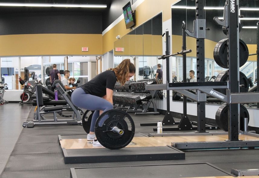 Marketing para academia: imagem de uma academia com um mulher levantando peso e outras pessoa no fundo em outros aparelhos