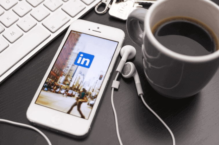 o que é linkedin: imagem de um celular com fone de ouvido plugado em cima de uma mesa com a tela do linkedin aberta e uma xícara de café ao lado