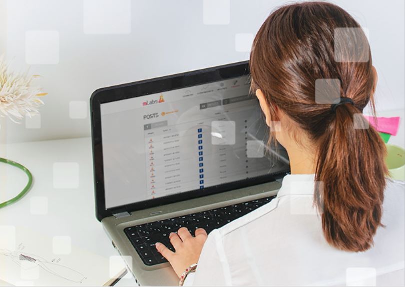 postagem automatica instagram: imagem de uma mulher sentada digitando em um notebook com a página de posts da mLabs aparecendo na tela|||||||||||
