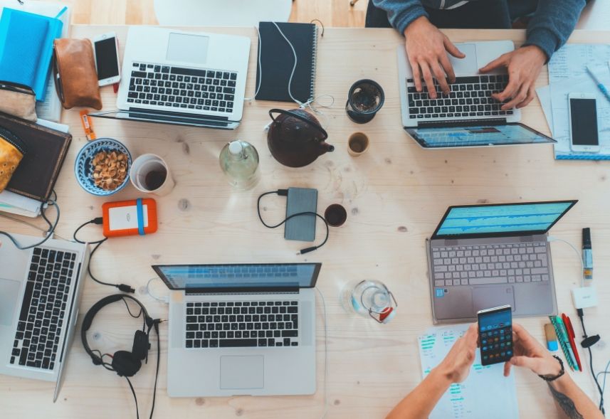 Social Ads: imagem de uma mesa de trabalho com quatro notebooks abertos duas pessoas trabalhando